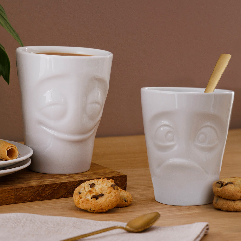 Set of two coffee mugs without handles in white from the porcelain product family of fun dishware by FIFTYEIGHT Products. Each offering 11 oz capacity. Dishwasher and microwave safe coffee cups with 'Cheery' and 'Baffled' facial expression. Shipped in exclusively designed gift box.