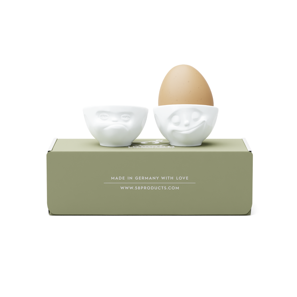 Set of two egg cups in white from the porcelain product family of fun dishware by FIFTYEIGHT Products. Set features two egg cups in white, featuring 'Happy' and 'Hmpff' facial expressions. Dishwasher and microwave safe bowls. Shipped in exclusively designed gift box.