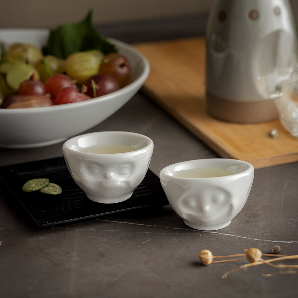 Set of two egg cups in white from the porcelain product family of fun dishware by FIFTYEIGHT Products. Set features two egg cups in white, featuring 'Happy' and 'Hmpff' facial expressions. Dishwasher and microwave safe bowls. Shipped in exclusively designed gift box.