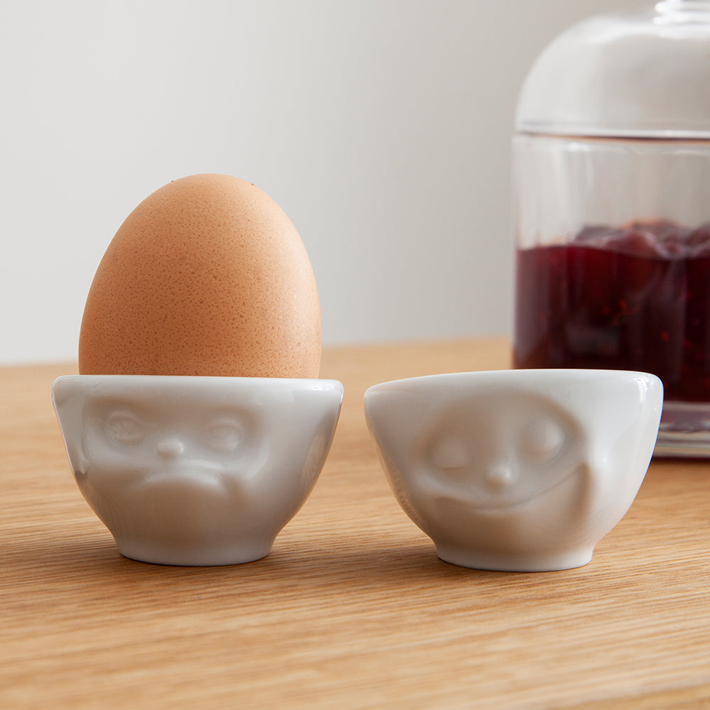 Set of two egg cups in white from the porcelain product family of fun dishware by FIFTYEIGHT Products. Set features two egg cups in white, featuring 'Happy' and 'Hmpff' facial expressions. Dishwasher and microwave safe bowls. Shipped in exclusively designed gift box.