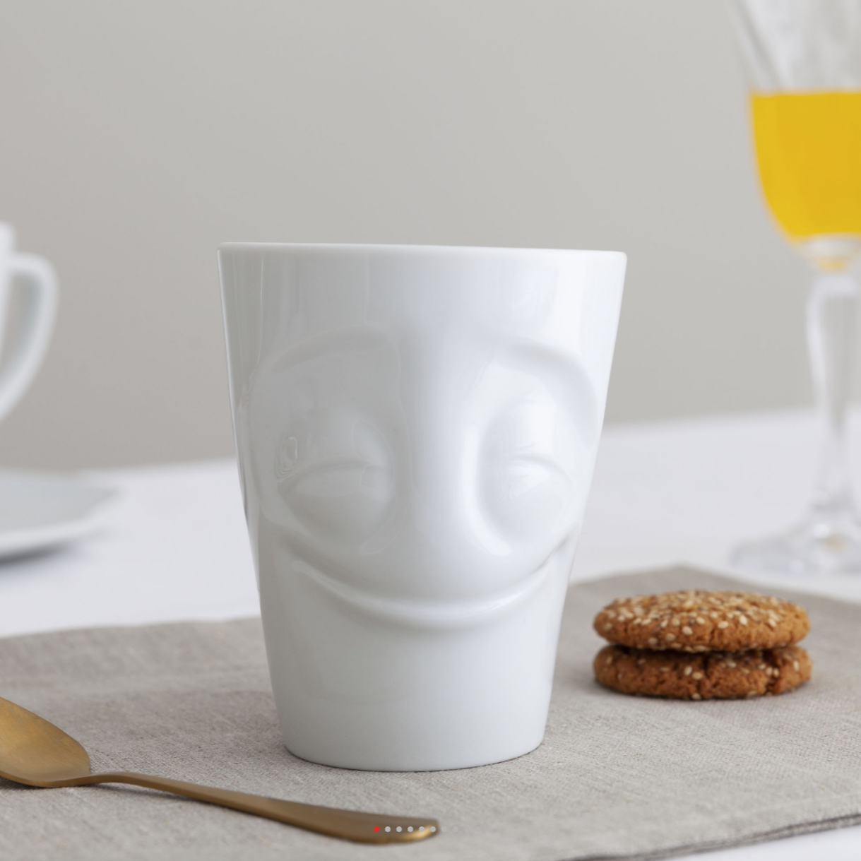 Coffee mug with 'cheery' facial expression and 11 oz capacity. From the TASSEN product family of fun dishware by FIFTYEIGHT Products. Tall coffee cup with handle in white, crafted from quality porcelain.