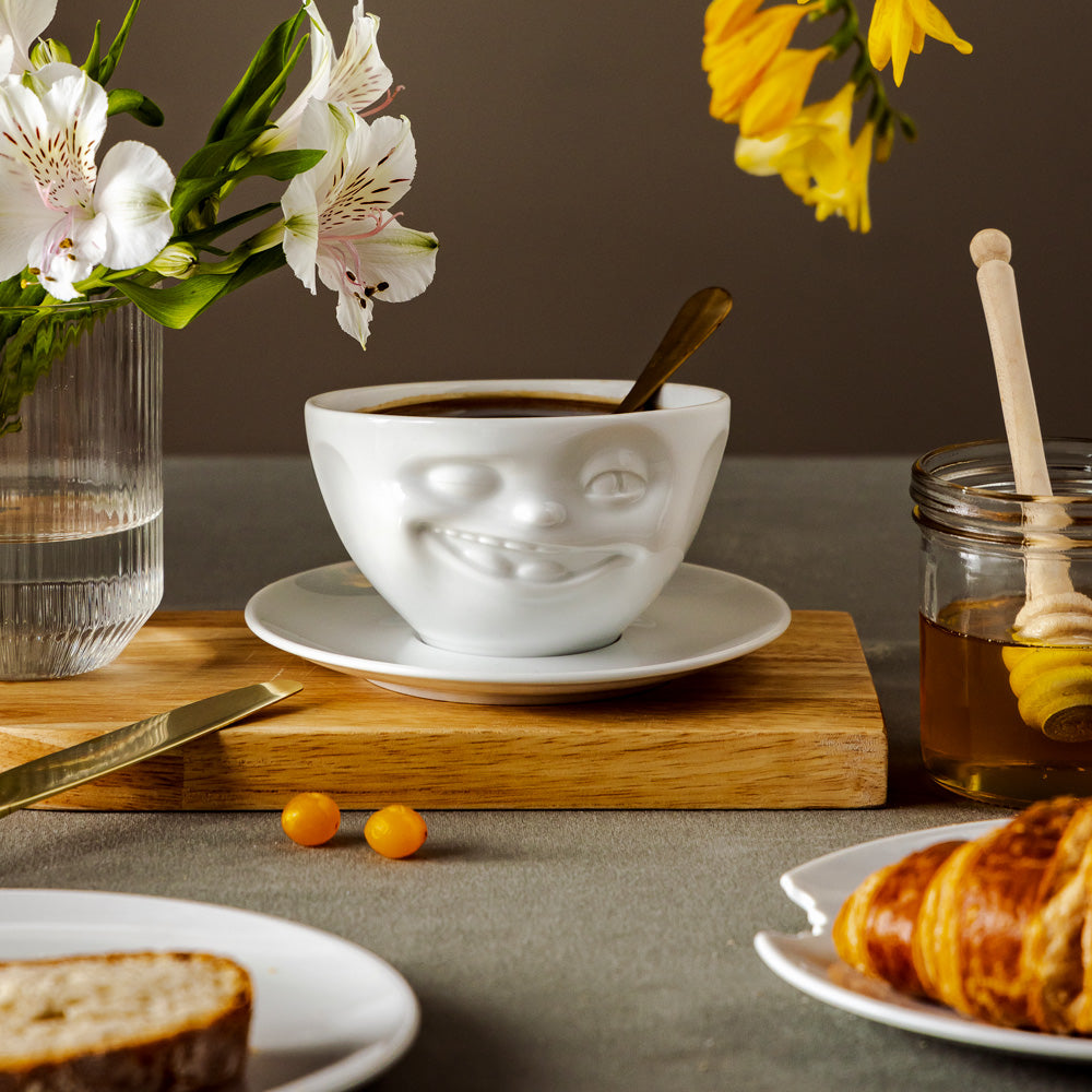 Premium porcelain coffee cup with saucer in white from the porcelain product family of fun dishware by FIFTYEIGHT Products. Offers 6.5 oz capacity and comes with a matching saucer. Dishwasher and microwave safe cup with a 'laughing' facial expression. Shipped in exclusively designed gift box.