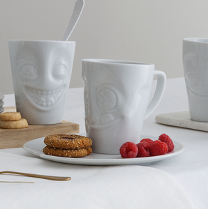 Coffee mug with 'tasty' facial expression and 11 oz capacity. From the TASSEN product family of fun dishware by FIFTYEIGHT Products. Tall coffee cup with handle in white, crafted from quality porcelain.