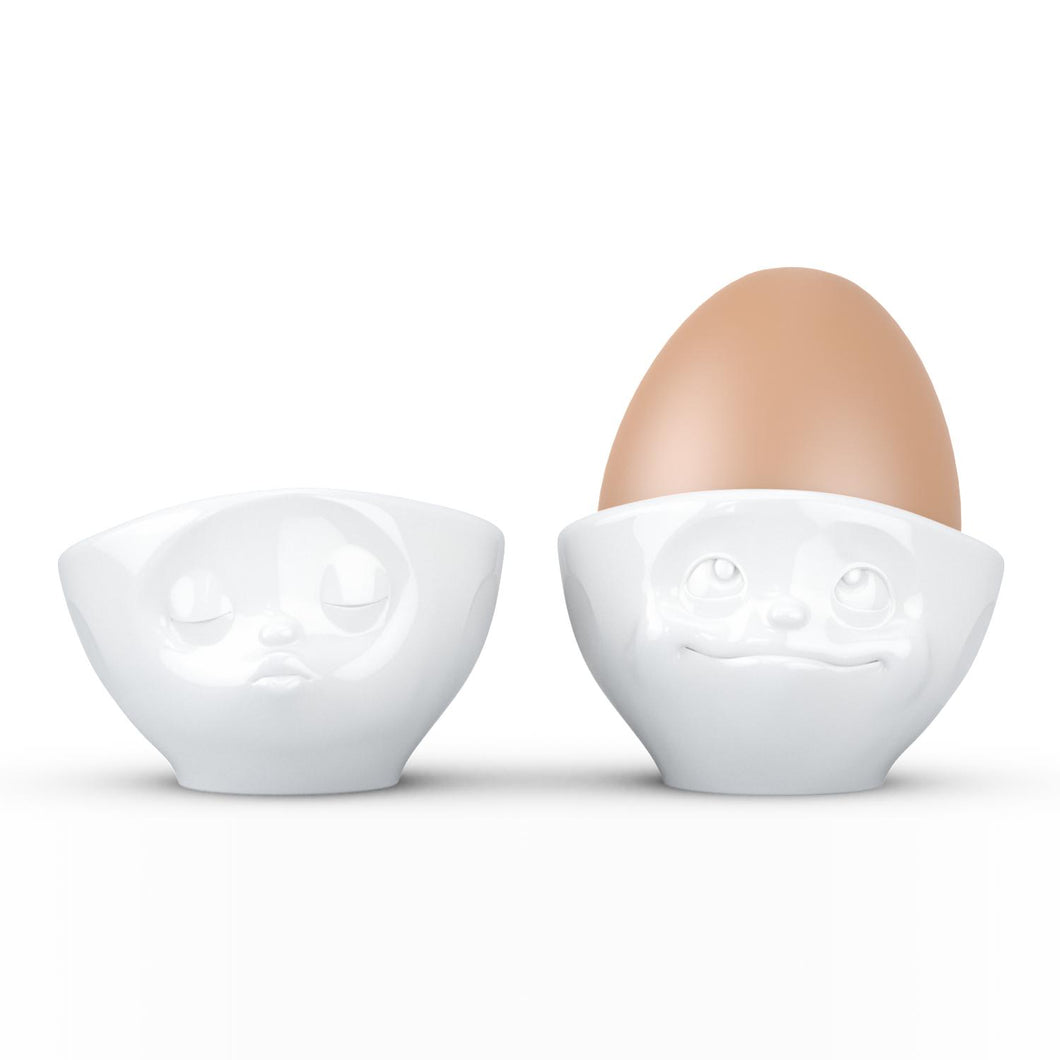 Set of two egg cups in white from the TASSEN product family of fun dishware by FIFTYEIGHT Products. Set features two egg cups in white, featuring 'kissing' and 'dreamy' facial expressions. Dishwasher and microwave safe bowls. Shipped in exclusively designed gift box.