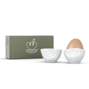 Set of two egg cups in white from the TASSEN product family of fun dishware by FIFTYEIGHT Products. Set features two egg cups in white, featuring 'Oh please' and 'tasty' facial expressions. Dishwasher and microwave safe bowls. Shipped in exclusively designed gift box.
