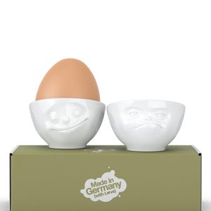 Set of two egg cups in white from the TASSEN product family of fun dishware by FIFTYEIGHT Products. Set features two egg cups in white, featuring 'Happy' and 'Hmpff' facial expressions. Dishwasher and microwave safe bowls. Shipped in exclusively designed gift box.