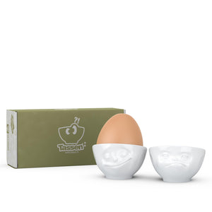 Set of two egg cups in white from the TASSEN product family of fun dishware by FIFTYEIGHT Products. Set features two egg cups in white, featuring 'Happy' and 'Hmpff' facial expressions. Dishwasher and microwave safe bowls. Shipped in exclusively designed gift box.